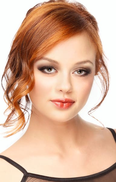 Strawberry to auburn red hair color hues on updo with wavy face-framing loose tendrils.