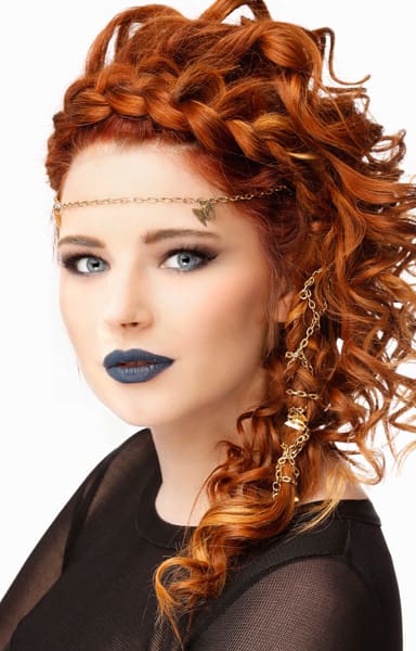 Rich coppery red hair highlighted with strawberry tones accent the face crowning braid and side swept long curls.